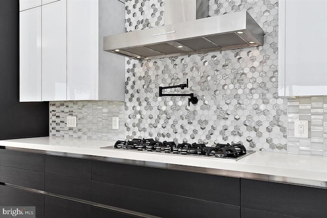 kitchen featuring white cabinets, decorative backsplash, stainless steel gas stovetop, and wall chimney range hood