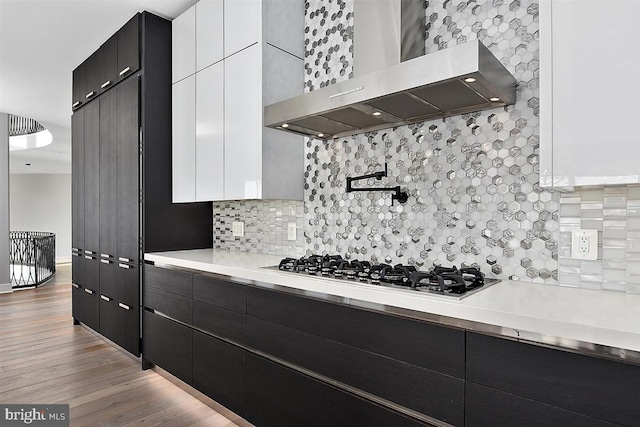 kitchen with white cabinetry, wall chimney exhaust hood, light hardwood / wood-style floors, and stainless steel gas cooktop