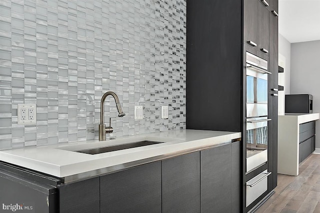 kitchen featuring stainless steel double oven, decorative backsplash, sink, and light hardwood / wood-style floors