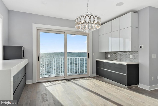 kitchen with white cabinetry, hanging light fixtures, an inviting chandelier, light hardwood / wood-style flooring, and a water view