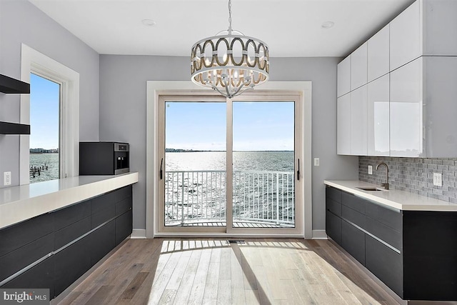 unfurnished dining area with a chandelier, a water view, light hardwood / wood-style floors, and sink