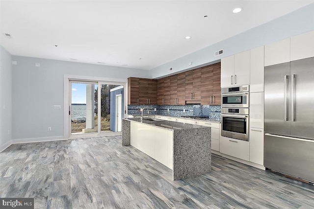 kitchen with backsplash, light hardwood / wood-style flooring, dark stone countertops, white cabinetry, and stainless steel appliances