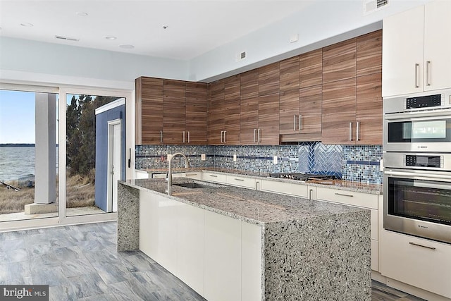 kitchen with white cabinetry, sink, stainless steel appliances, tasteful backsplash, and a water view