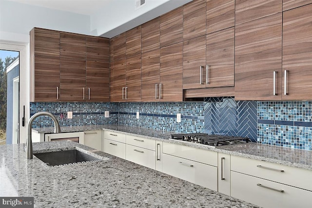 kitchen with backsplash, light stone countertops, sink, and stainless steel gas stovetop