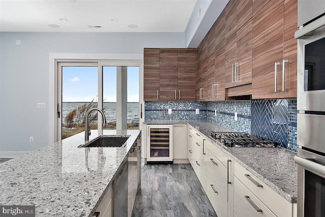 kitchen featuring a water view, sink, appliances with stainless steel finishes, light stone counters, and beverage cooler