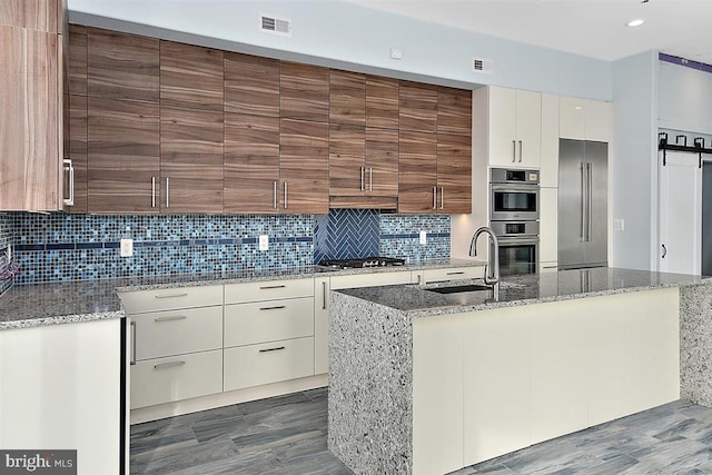 kitchen with light stone countertops, appliances with stainless steel finishes, dark hardwood / wood-style flooring, sink, and a center island with sink