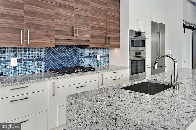 kitchen with light stone countertops, sink, backsplash, white cabinets, and appliances with stainless steel finishes