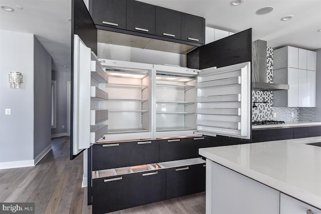 kitchen with hardwood / wood-style floors, stainless steel gas stovetop, wall chimney range hood, decorative backsplash, and white cabinetry