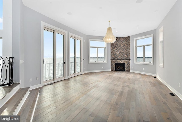 unfurnished living room featuring a fireplace, a water view, a healthy amount of sunlight, and wood-type flooring