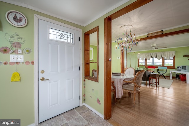 entryway with crown molding, ceiling fan with notable chandelier, and light tile flooring