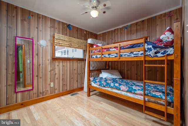 bedroom with light hardwood / wood-style floors, ornamental molding, wooden walls, and ceiling fan