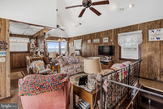 living room featuring wood walls, lofted ceiling, and ceiling fan with notable chandelier