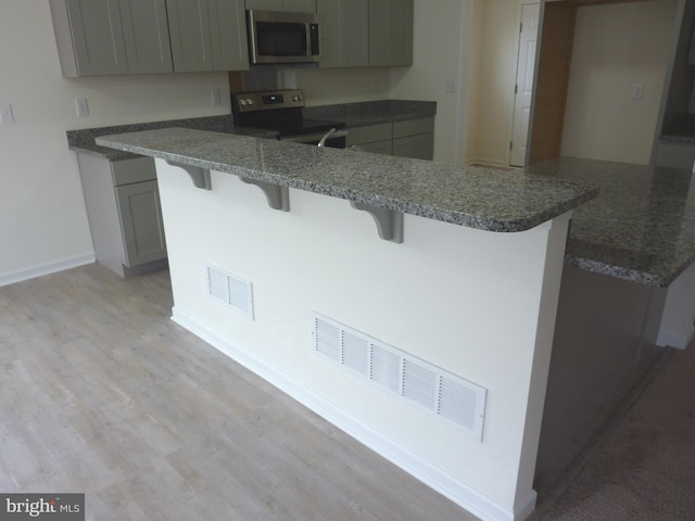 kitchen featuring a breakfast bar, gray cabinetry, light hardwood / wood-style floors, and range with electric stovetop