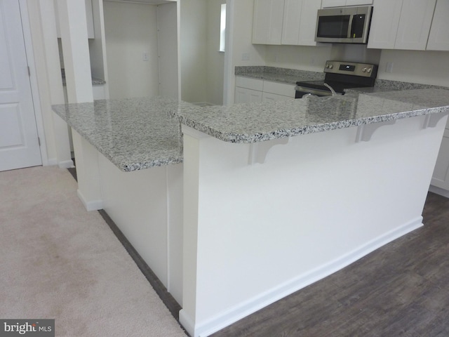 kitchen with appliances with stainless steel finishes, white cabinetry, a breakfast bar area, kitchen peninsula, and light stone countertops