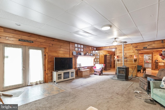 living room featuring a paneled ceiling, light carpet, ceiling fan, and a wood stove