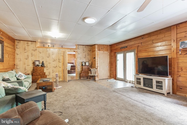 unfurnished living room featuring ceiling fan, wooden walls, light carpet, and french doors