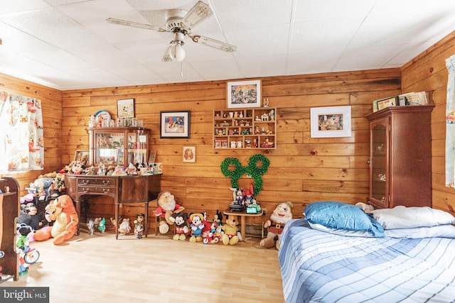 bedroom with ceiling fan, a drop ceiling, wood walls, and light hardwood / wood-style floors