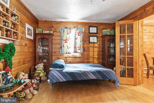 bedroom featuring a paneled ceiling, light wood-type flooring, and wooden walls