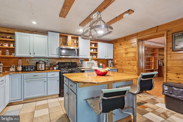 kitchen featuring light tile floors, black stove, a kitchen breakfast bar, butcher block counters, and wood walls