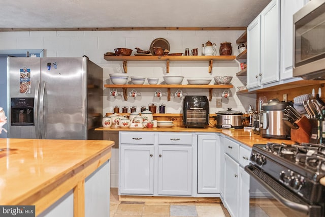 kitchen with light tile floors, white cabinets, wood counters, and stainless steel appliances