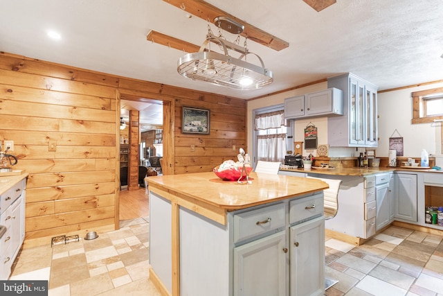 kitchen with light tile flooring, wood walls, a kitchen island, and a textured ceiling