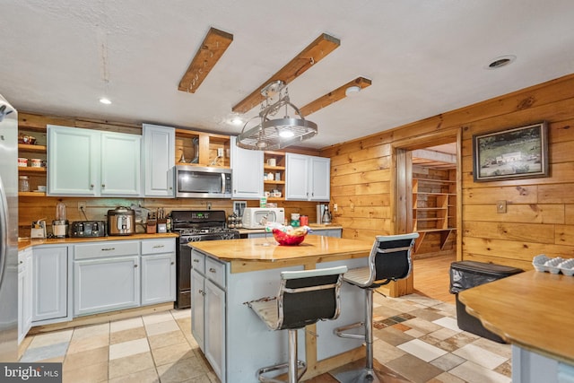 kitchen featuring a kitchen bar, wooden counters, black stove, pendant lighting, and light tile flooring