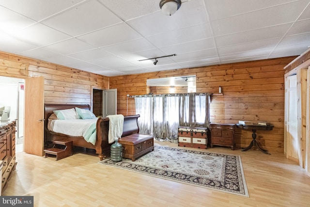 bedroom featuring a paneled ceiling, wood walls, and light hardwood / wood-style flooring