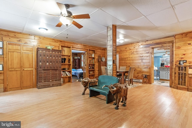 game room featuring ceiling fan, a paneled ceiling, light wood-type flooring, and wooden walls