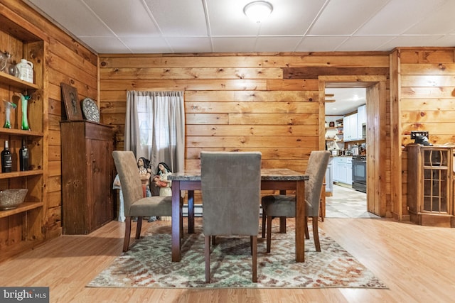 dining area with a paneled ceiling, light wood-type flooring, wood walls, and a baseboard heating unit