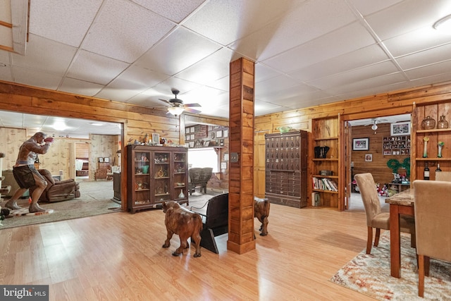 dining area with wooden walls, ceiling fan, a drop ceiling, and light hardwood / wood-style floors