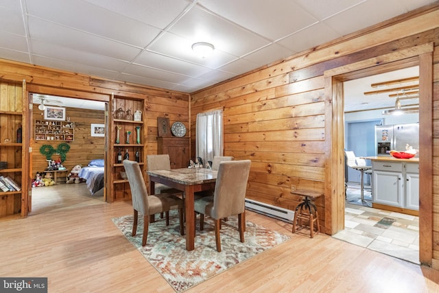 dining space with a paneled ceiling, wooden walls, light hardwood / wood-style floors, and a baseboard heating unit