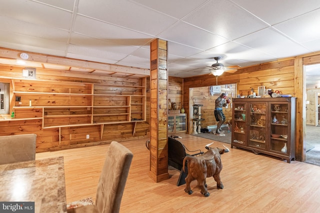 dining room featuring ceiling fan, wood walls, a drop ceiling, and light hardwood / wood-style floors