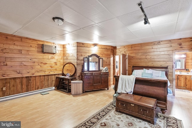 bedroom featuring a paneled ceiling, wood walls, a wall mounted AC, a baseboard heating unit, and light hardwood / wood-style flooring