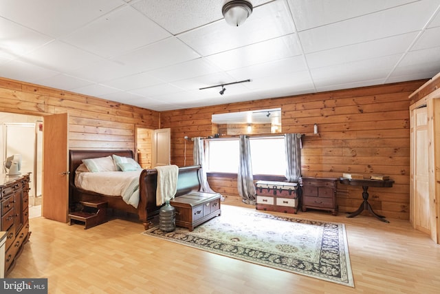 bedroom with wood walls, a drop ceiling, and light hardwood / wood-style flooring