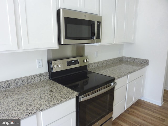 kitchen with appliances with stainless steel finishes, light wood-type flooring, light stone counters, and white cabinets