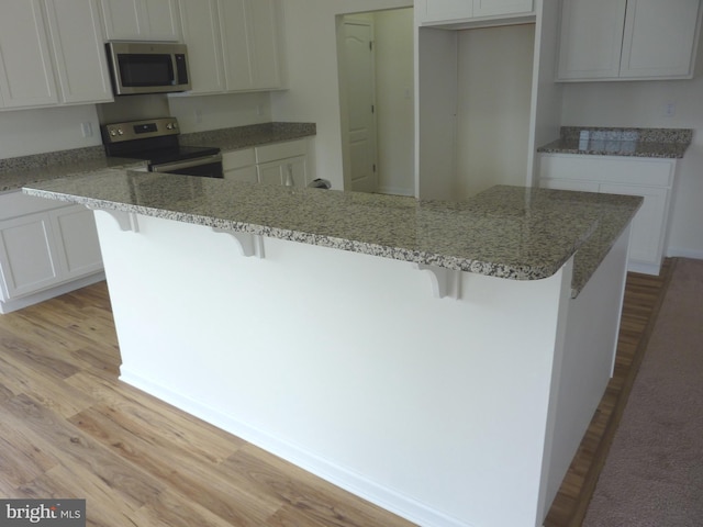 kitchen featuring stainless steel appliances, light wood-type flooring, a kitchen bar, and light stone counters