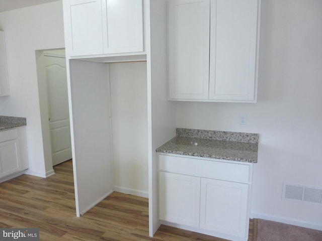 kitchen featuring hardwood / wood-style floors, white cabinets, and light stone counters