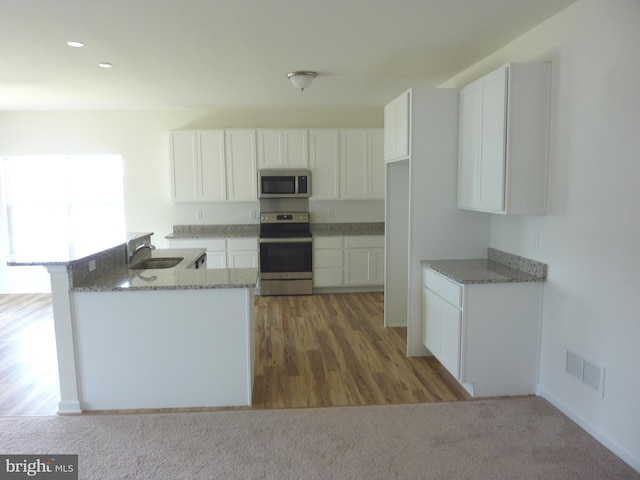 kitchen featuring white cabinets, appliances with stainless steel finishes, light carpet, and light stone counters