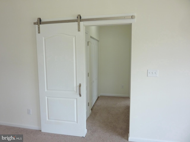 corridor featuring a barn door and light colored carpet