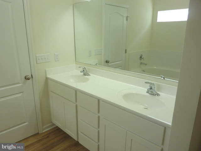 bathroom with a bath to relax in, wood-type flooring, double sink, and vanity with extensive cabinet space