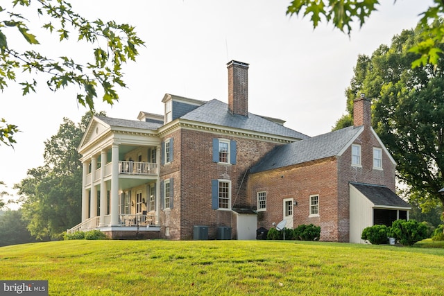 view of front of house with central air condition unit, a balcony, and a front lawn