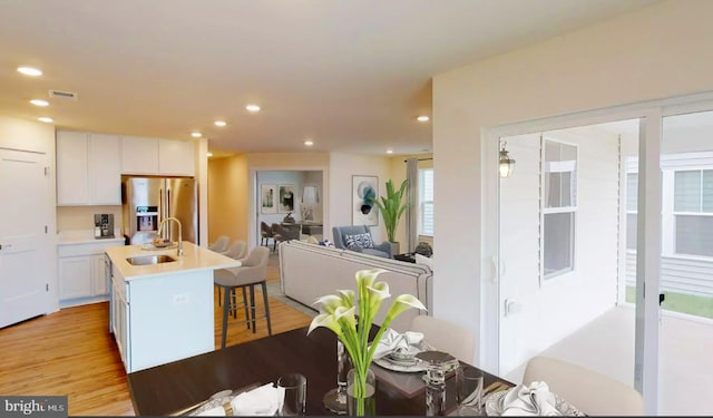 kitchen featuring white cabinetry, a center island with sink, light wood-type flooring, stainless steel fridge, and sink