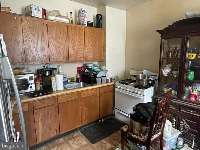 kitchen with white gas range oven, sink, and stainless steel refrigerator