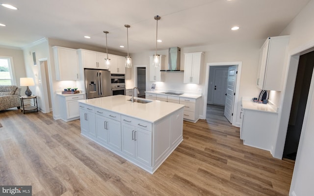 kitchen with decorative light fixtures, white cabinetry, an island with sink, stainless steel appliances, and wall chimney exhaust hood