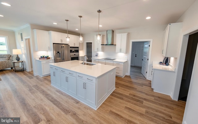 kitchen featuring wall chimney range hood, a center island with sink, pendant lighting, white cabinetry, and appliances with stainless steel finishes