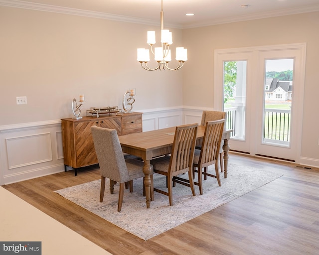 dining area with light hardwood / wood-style floors, ornamental molding, and an inviting chandelier