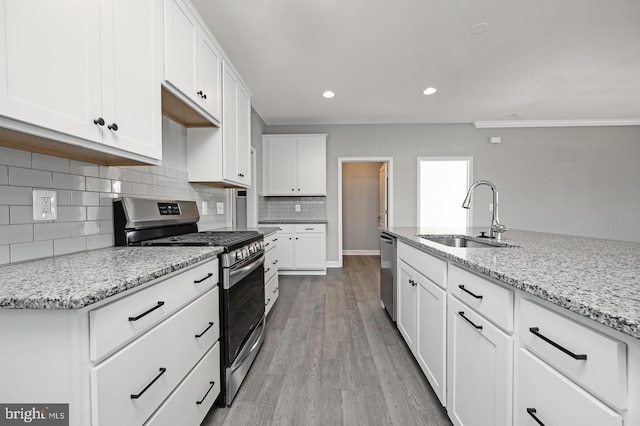 kitchen with light hardwood / wood-style floors, sink, white cabinetry, appliances with stainless steel finishes, and light stone counters