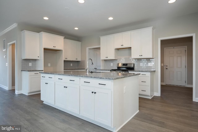 kitchen with white cabinets, wood-type flooring, dark stone counters, stainless steel stove, and a kitchen island with sink