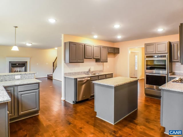 kitchen featuring stainless steel appliances, decorative light fixtures, a center island, light stone countertops, and dark hardwood / wood-style floors