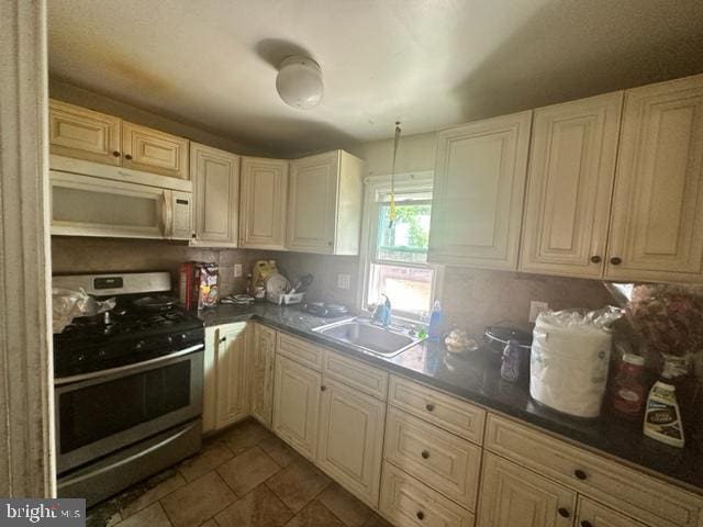 kitchen featuring sink, stainless steel range with gas cooktop, backsplash, and dark tile floors